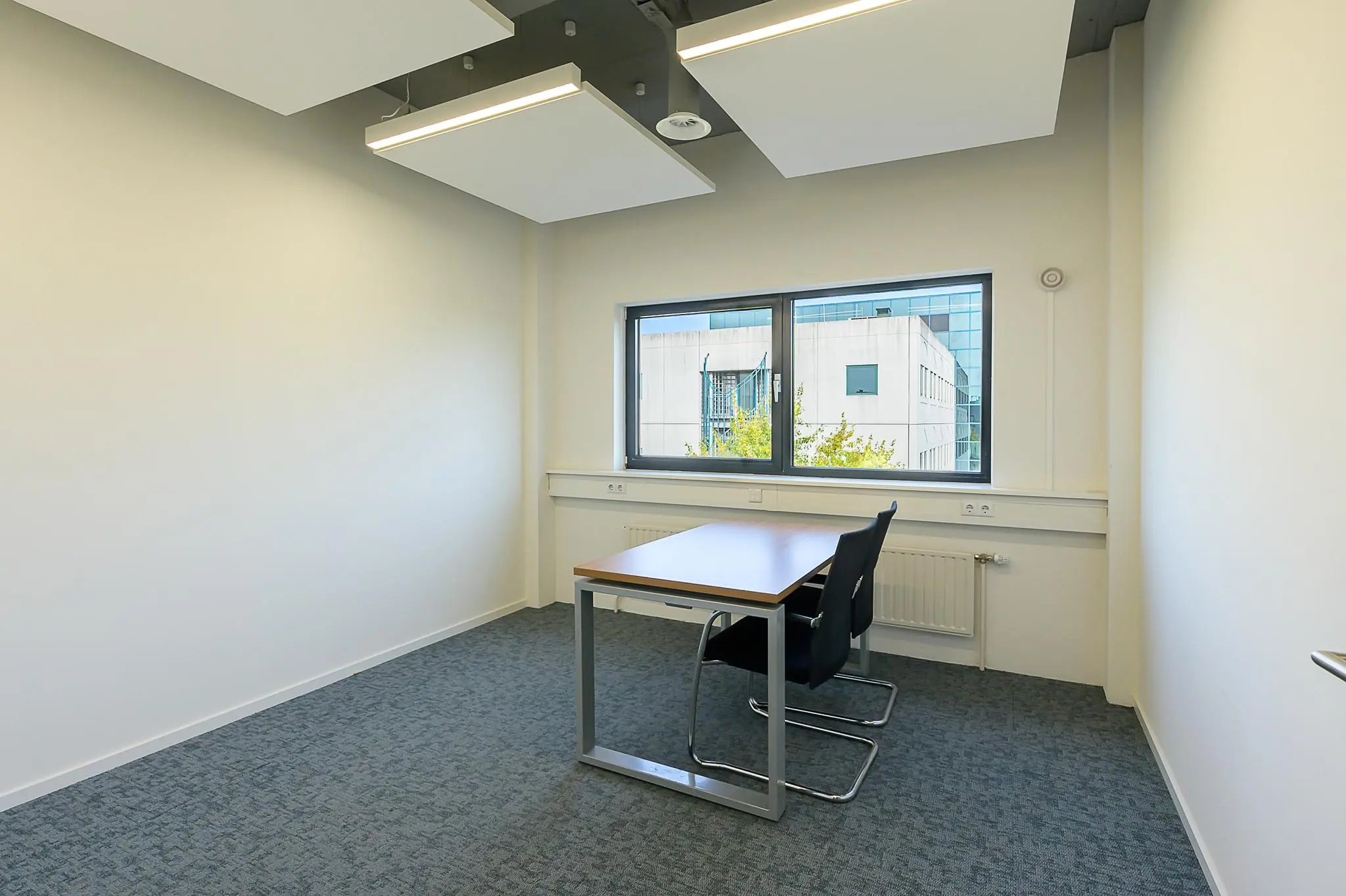 Kleine, moderne kantoorruimte aan de K.P. van der Mandelelaan met een bureau, twee stoelen en uitzicht op een kantoorgebouw.